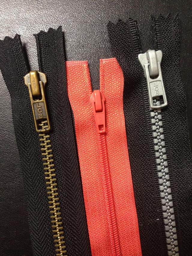 Close-up of three zippers: brass, red plastic coil and grey moulded plastic